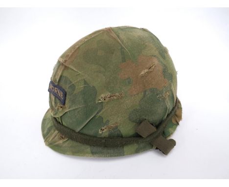 A US Vietnam war era helmet with camouflage cover, the chinstrap with applied Socialist Republic of North Vietnam badge