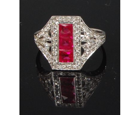 A white metal ruby and diamond dress ring, arranged as three square cut rubies each weighing approx 0.25ct, in a surround of 