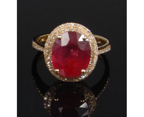 A contemporary 14ct yellow gold ruby and diamond dress ring, the oval cut ruby weighing 5.65ct, in a two-tier surround of sma