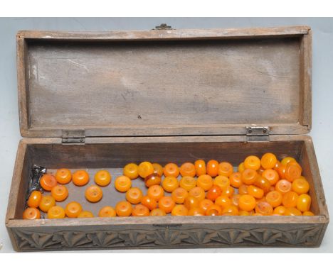 A collection of vintage 20th century amber coloured necklace beads, set within a carved wooden box. Likely plastic. Measures 