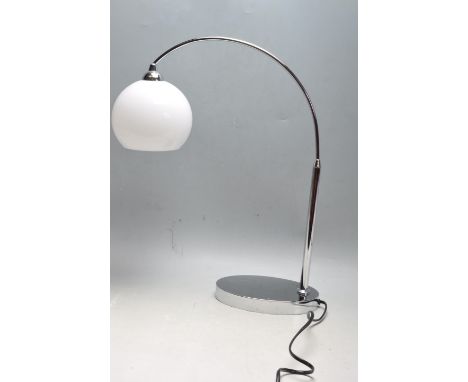 A contemporary retro style desk / side lamp having a globular milk glass shade suspended from a chrome arched arm raised on a