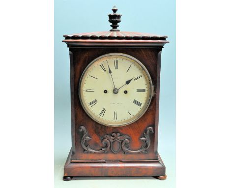 A Georgian early 19th century mahogany bracket clock having a finial top over a white enamel face, Roman numerals to the chap