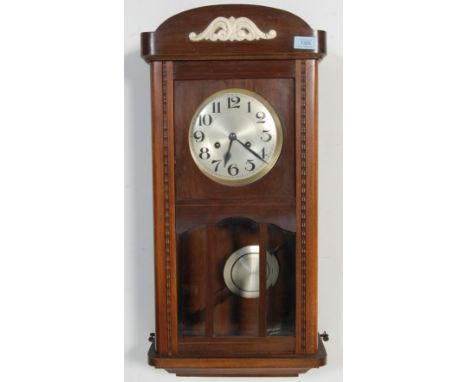 A mid century oak case eight day wall hanging clock having silver dial with Arabic numerals to the chapter ring, brass ring a