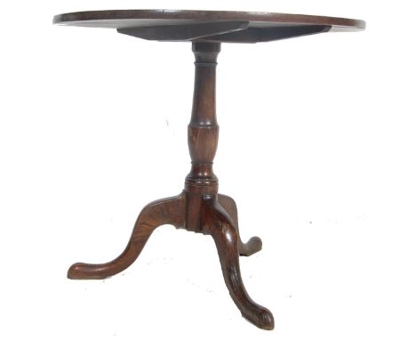 A Georgian early 19th century oak tilt top dining table having a circular top over gun barrel column raised on splayed tripod