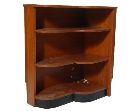 A vintage 1970’s teak wood corner cabinet bookcase shelf of scalloped shape having two fixed shelves raised on an ebonised pl