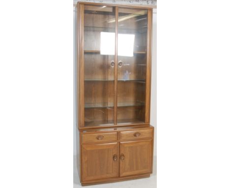 Ercol - Lucian Ercolani - An Ercol elm bookcase cabinet vitrine having twin glazed doors opening to reveal a shelved interior