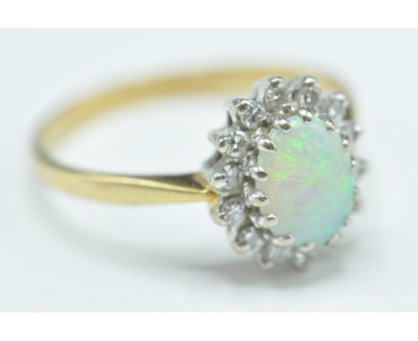 A hallmarked 18ct gold opal and diamond ring having a central oval opal panel with a halo of round cut diamond accent stones.