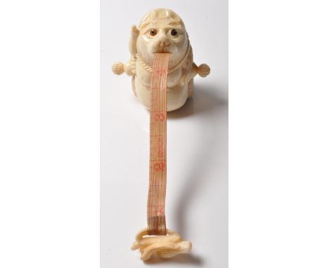 A unusual vintage style carved bone tape measure having a red stones to the eyes, winder handles to the side &amp; tape emana