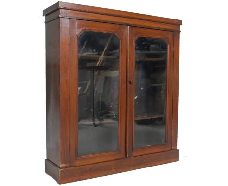 A Victorian 19th century mahogany bookcase cabinet being raised on a plinth base with twin glass doors housing shelves set wi