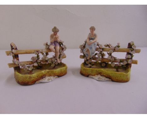 A pair of Sitzendorf figurines of a boy playing pipes and a girl sitting on a fence