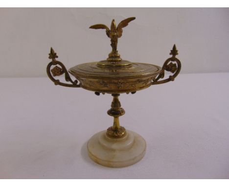 A brass tazza of classical form with bird finial, scroll handles on raised circular marble stand