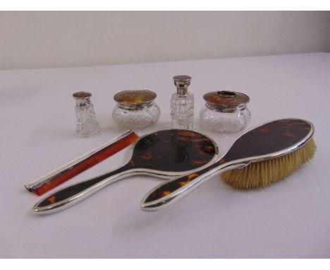 A quantity of tortoiseshell and silver dressing table pieces to include a hand mirror, a hair brush, four cut glass bottles w