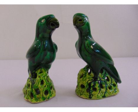 A pair of ceramic figurines of parrots on raised naturalistic bases