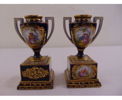 A pair of continental ceramic vases with pierced side handles on square plinths decorated with courting couples, A/F