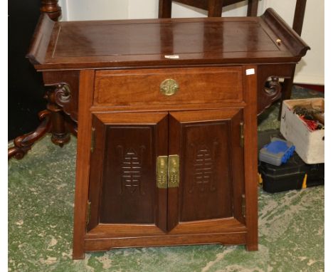 A Chinese hardwood altar cabinet, rectangular top with scroll ends above a drawer and a pair of doors, carved in relief with 