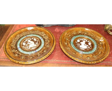 A pair of Clément Massier wall plaque chargers, relief decorated with a central figure of satyr upon a ribbon bench, double l