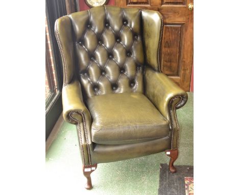 A wingback arm chair, green leather button upholstery.