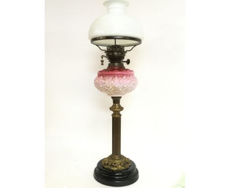 A late 19th century brass oil lamp with pink glass and a milk glass shade, approximately 67cm tall. This lot cannot be posted