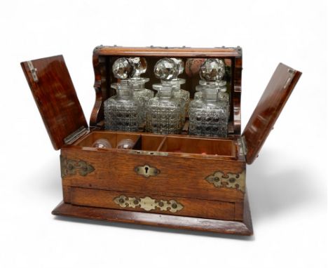 AN OAK TANTALUS BOX with three cut glass hobnail decanters, the case with former silver-plated brass mounts, the front openin