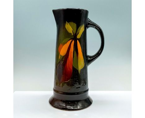 A glazed ceramic pitcher that painted in a color gradient of brown, green, and amber with banana leaves painted to the center