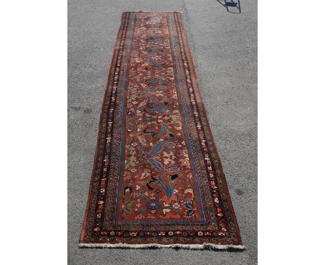 A large and decorative Northwest Persian runner, madder ground with stylised fronds, 560 x 130cm. Provenance: From Munstead W