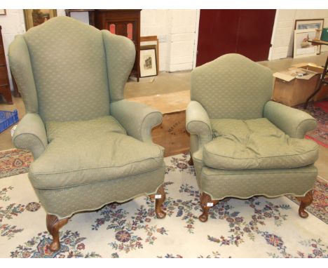 An Edwardian upholstered wing-back armchair with loose cushion, on carved short cabriole front legs and a matching smaller ar