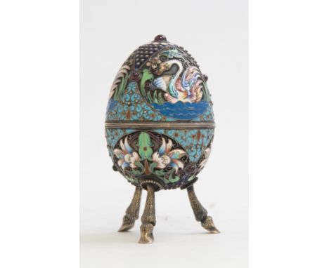 A Russian silver gilt and cloisonné enamelled egg, on three cast hoof legs, three champleve enamel swans, below foliate carto