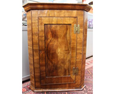 A 19th Century Georgian style walnut quarter veneered hanging corner cupboard, the panelled door enclosing a single drawer an