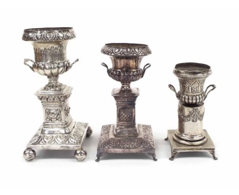 Three similar Continental white metal urns, repousse foliate decorated ,upon stepped square pillar supports raised on four le