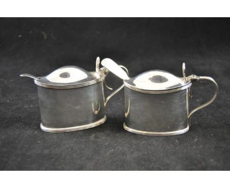 Two near matching silver mustard pots of oval shape with shell thumb pieces, Sheffield 1899 and Birmingham 1913, maker Willia