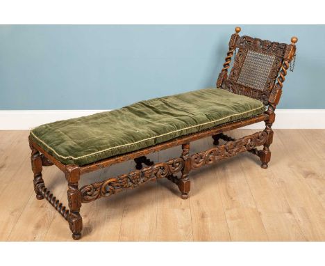 A Carolean style carved oak daybed, with cherub and foliate detail, barley twist supports and caned sloped backrest and seat.