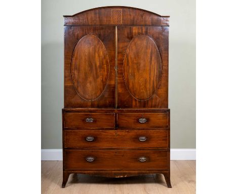 A Regency mahogany linen press with arching cornice over twin-panelled oval doors enclosing hanging space within and on a pos