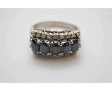 A ladies 18ct white gold ring, having a single row of five oval cut blue sapphires with diamond surround. 