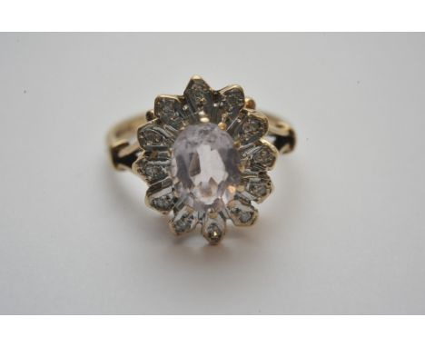 A ladies 9ct gold ring set with a central oval cut pink stone with diamond chip set surround