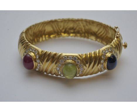 An impressive 18ct yellow gold bangle set with sapphire, ruby and sapphire cabochons with diamond surround