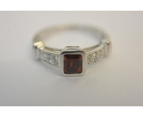 A ladies 18ct white gold ring set with an emerald cut ruby, or garnet, with diamond set shoulders