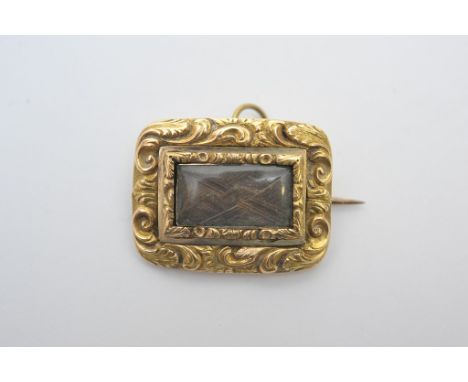 An antique gold mourning broach with ornate surround, the centre of which having entwined hair behind glass, also possesses a