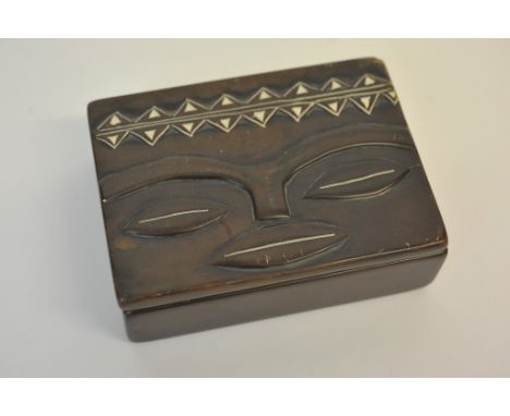 A bronze tribal art box and cover decorated in low relief with a face and above with a frieze of triangular shapes.