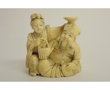 An oriental one piece ivory carving in the form of two seated figures holding a kettle