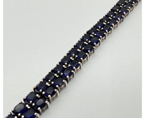 A double row tennis style silver bracelet set with oval cut dark blue glass stones. Approx 7.5 inches long. Approx. 39.7g 