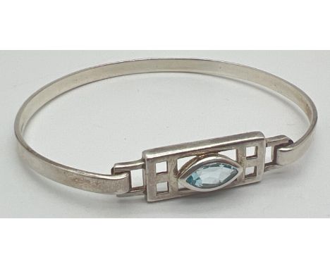 A modern design silver bangle with Rennie Mackintosh style pierced work panel set with a marquise cut blue topaz. Hook fixing