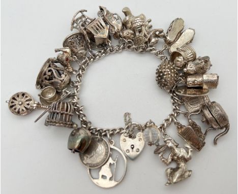 A vintage silver charm bracelet with padlock, safety chain and 27 silver and white metal charms. Many charms open to reveal i