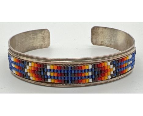 A Native American silver bangle with multi coloured small glass bead work panel set to front. Makers marks and Sterling mark 