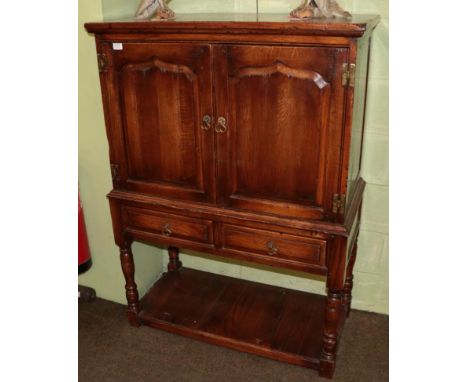 An oak cupboard, modern, with moulded doors enclosing a divided shelf, two frieze drawers below, on turned baluster legs join