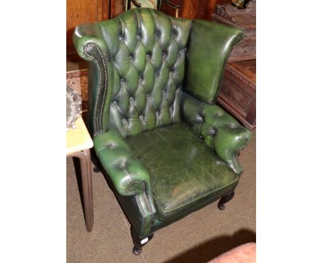 A Georgian style buttoned green leather wing back armchair 