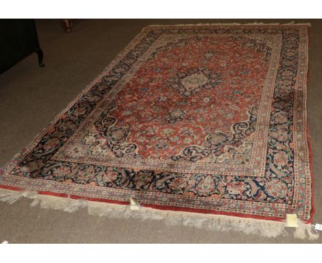 Indian carpet of Kashan design, the terracotta field of vines centred by an indigo medallion framed by spandrels and indigo b