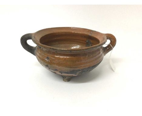 Medieval glazed pot, circa 15th century, with twin loop handles and standing on tripod feet, 28.5cm across including handlesS