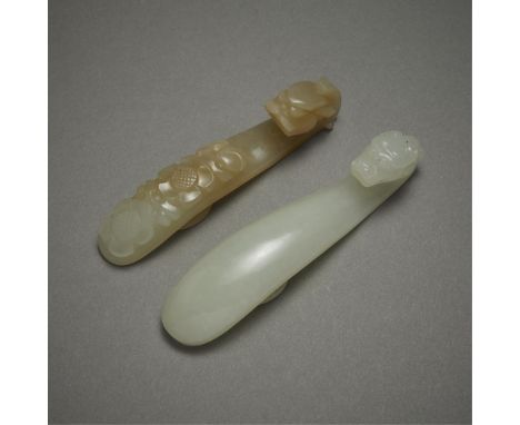 Group of two Chinese carved jade belt hooks. One of a pale yellow-green coloration with floral decoration carved along the lo