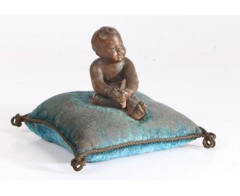 A 19th century French pin cushion, the turquoise cushion surmounted by a terracotta depiction of a seated child, 13cm square