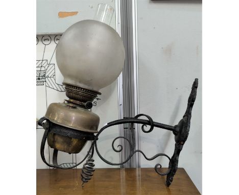 A brass and wrought iron oil lamp, wall mounted, with shade 